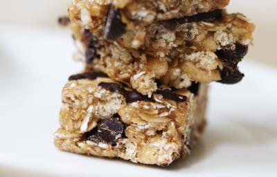 Fotografia de barrinhas de cereal de mel com aveia cobertas por chocolate. As barrinhas estão uma sobre a outra.