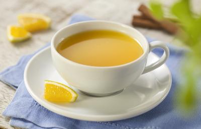 Fotografia em tons de azul, cinza e amarelo de uma bancada cinza com um paninho azul e sobre ele um prato branco redondo com uma xícara com chá de laranja. Ao fundo paus de canela e pedaços de laranja. Fotografia em tons de azul, cinza e amarelo de uma bancada cinza com um paninho azul e sobre ele um prato branco redondo com uma xícara com chá de laranja. Ao fundo paus de canela e pedaços de laranja.