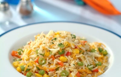 Prato de porcelana branco com porção de arroz colorido com milho, ervilha, cenoura ralada e coentro picado.