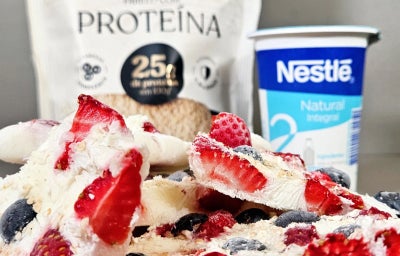 Pedaços de iogurte congelado com morangos e mirtilos sobre prato de madeira, com produtos Nestlé ao fundo.