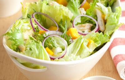 em uma mesa de madeira contém um recipiente branco que comporta a salada. Ao lado um pote com tempero e um pano listrado nas cores branco e rosa. em uma mesa de madeira contém um recipiente branco que comporta a salada. Ao lado um pote com tempero e um pano listrado nas cores branco e rosa.