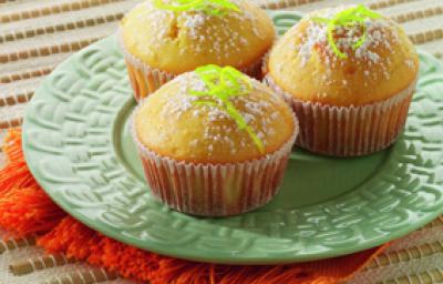 Fotografia em tons de verde, branco e amarelo, ao centro prato verde sobre guardanapo laranja, com três bolinhos decorados com raspas de laranja e açúcar, tudo sobre toalha branca alinhavada. Fotografia em tons de verde, branco e amarelo, ao centro prato verde sobre guardanapo laranja, com três bolinhos decorados com raspas de laranja e açúcar, tudo sobre toalha branca alinhavada.