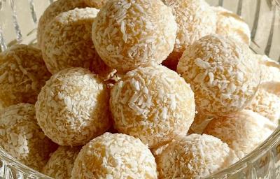 Fotografia em tons de branco com um pote de vidro ao centro. Dentro do pote existe várias unidades de brigadeiro de chocolate branco finalizados com coco ralado Fotografia em tons de branco com um pote de vidro ao centro. Dentro do pote existe várias unidades de brigadeiro de chocolate branco finalizados com coco ralado