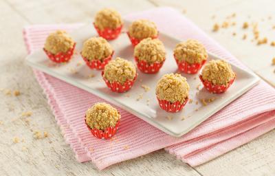 Fotografia em tons de branco e vermelho de bancada de madeira branca, pano rosa dobrado, um brigadeiro de paçoca sobre o pano, prato retangular branco com nove brigadeiros de paçoca em forminhas vermelhas com bolinhas brancas. Fotografia em tons de branco e vermelho de bancada de madeira branca, pano rosa dobrado, um brigadeiro de paçoca sobre o pano, prato retangular branco com nove brigadeiros de paçoca em forminhas vermelhas com bolinhas brancas.