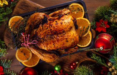A imagem mostra um frango inteiro assado, decorado com fatias de laranja. A imagem de fundo remete ao Natal, com bolas vermelhas e festão A imagem mostra um frango inteiro assado, decorado com fatias de laranja. A imagem de fundo remete ao Natal, com bolas vermelhas e festão
