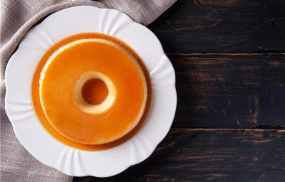 A foto descreve um pudim em um prato branco em uma mesa de madeira A foto descreve um pudim em um prato branco em uma mesa de madeira