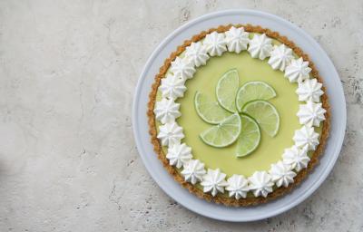 Foto de uma torta limão em cima de um prato branco e com fatias de limão decorando o centro da torta. Foto de uma torta limão em cima de um prato branco e com fatias de limão decorando o centro da torta.