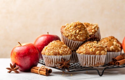 Muffins de maçã com cobertura crocante, sobre grade metálica, acompanhados de maçãs e canela.