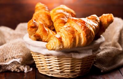 Fotografia de cestinhas de palha com um pano de tom bege. Dentro da cestinha no centro da foto, tem vários pães tipo croissant. Fotografia de cestinhas de palha com um pano de tom bege. Dentro da cestinha no centro da foto, tem vários pães tipo croissant.