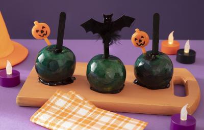 Foto da receita de maçã do amor da bruxa malvada servida em 3 porções sobre uma tábua de madeira com decoração de halloween em volta