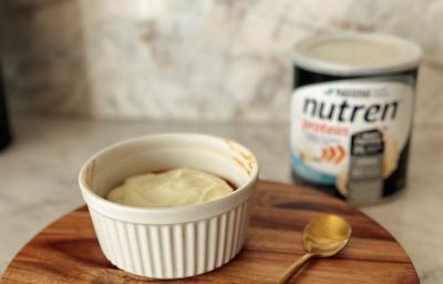 Foto da receita de cookie de airfryer feito com Nutren Protein, servido e um pote branco com uma cobertura branca por cima e a lata do produto ao fundo Foto da receita de cookie de airfryer feito com Nutren Protein, servido e um pote branco com uma cobertura branca por cima e a lata do produto ao fundo