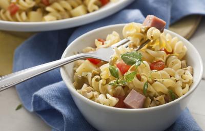 Fotografia em tons de azul em uma bancada de madeira com um pano azul ao fundo, um prato redondo fundo com a salada de macarrão tipo parafuso, com bacon e tomate. Fotografia em tons de azul em uma bancada de madeira com um pano azul ao fundo, um prato redondo fundo com a salada de macarrão tipo parafuso, com bacon e tomate.
