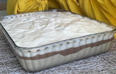 Fotografia em tons de amarelo em uma bancada de madeira com uma travessa de vidro e a torta de farinha láctea nestlé dentro.