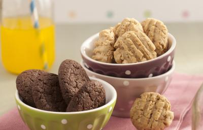 Fotografia em tons de rosa em uma bancada de madeira clara com potinhos verde, branco e marrom com bolinhas brancas em cima de um pano rosa e biscoitinhos de chocolate e aveia dentro dos potinhos. Fotografia em tons de rosa em uma bancada de madeira clara com potinhos verde, branco e marrom com bolinhas brancas em cima de um pano rosa e biscoitinhos de chocolate e aveia dentro dos potinhos.