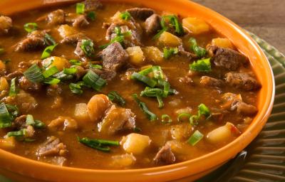 Foto aproximada de um prato marrom com a receita de carne de panela com mandioca dentro, em um caldo grosso e marrom, com pedaços de carne, mandioca e cheiro-verde picado Foto aproximada de um prato marrom com a receita de carne de panela com mandioca dentro, em um caldo grosso e marrom, com pedaços de carne, mandioca e cheiro-verde picado