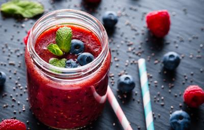 Fotografia de um copo de vidro decorativo sobre uma mesa preta, com frutas vermelhas e sementes de linhaça espalhadas ao lado de dois canudos. Dentro do copo tem um smoothie de frutas vermelhas com algumas blueberries e folhas de hortelã decorando. Fotografia de um copo de vidro decorativo sobre uma mesa preta, com frutas vermelhas e sementes de linhaça espalhadas ao lado de dois canudos. Dentro do copo tem um smoothie de frutas vermelhas com algumas blueberries e folhas de hortelã decorando.