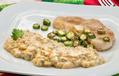 Fotografia em tons de verde em uma mesa com uma toalha verde florida, um prato branco grande com o peixe servido com quiabo e com purê de banana da terra. Fotografia em tons de verde em uma mesa com uma toalha verde florida, um prato branco grande com o peixe servido com quiabo e com purê de banana da terra.