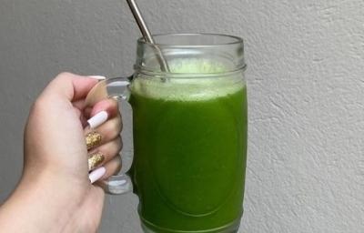 Fotografia de uma mão feminina segurando uma caneca de vidro grande com suco detox, de cor verde, com canudo de alumínio. Fotografia de uma mão feminina segurando uma caneca de vidro grande com suco detox, de cor verde, com canudo de alumínio.