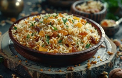 Em cima de uma mesa, tigela com porção de arroz dourado soltinho com uvas passas e nozes picadas. Em cima de uma mesa, tigela com porção de arroz dourado soltinho com uvas passas e nozes picadas.
