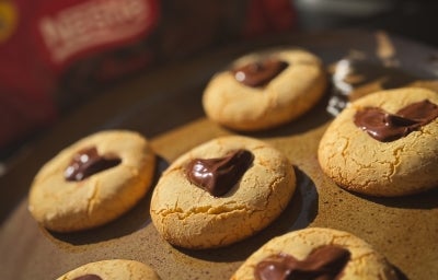 Fotografia de um prato grande e raso de tom marrom na frente da embalagem do chocolate classic meio amargo. Sobre o prato tem alguns sequilhos de leite em pó zero lactose com uma decoração de chocolate em formato de coração. Fotografia de um prato grande e raso de tom marrom na frente da embalagem do chocolate classic meio amargo. Sobre o prato tem alguns sequilhos de leite em pó zero lactose com uma decoração de chocolate em formato de coração.
