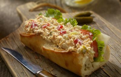 Fotografia de um sanduíche no pão francês com tomate, patê, queijo e alface, sobre uma tábua de madeira escura. Ao lado, uma faca com o cabo marrom. Fotografia de um sanduíche no pão francês com tomate, patê, queijo e alface, sobre uma tábua de madeira escura. Ao lado, uma faca com o cabo marrom.
