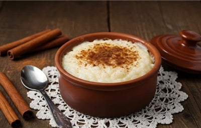 Em cima de uma mesa, tigela com arroz doce cremoso, com uma textura suave e aveludada, decorado com canela em pó.