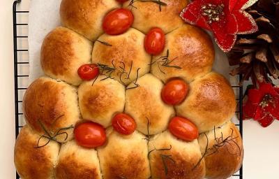 Foto da receita de Pão Caseiro Natalino. Observa-se um pão assado e dourado em formato de árvore, decorado com tomatinhos cereja Foto da receita de Pão Caseiro Natalino. Observa-se um pão assado e dourado em formato de árvore, decorado com tomatinhos cereja