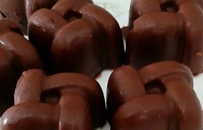 Fotografia de seis unidades de bombons recheados com banana e açaí, os quais estão sobre um prato branco. Fotografia de seis unidades de bombons recheados com banana e açaí, os quais estão sobre um prato branco.