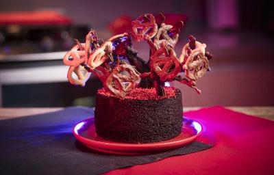 Bolo de chocolate decorado com galhos feitos de chocolate, formando uma árvore irregular onde ChocoPretzels ficam pendurados como pequenos frutos.