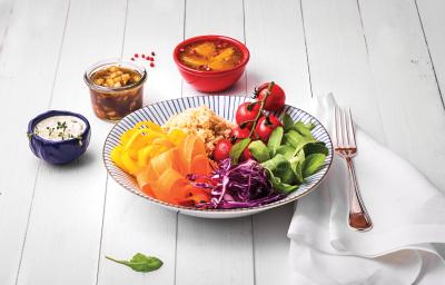 Fotografia em tons coloridos em uma bancada de madeira branca com um prato fundo com listras azuis e salada de rúcula, cenoura, cebola roxa e tomate dentro dele. Ao lado, potinhos com opções de molhos. Fotografia em tons coloridos em uma bancada de madeira branca com um prato fundo com listras azuis e salada de rúcula, cenoura, cebola roxa e tomate dentro dele. Ao lado, potinhos com opções de molhos.