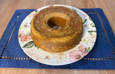 Fotografia de um bolo de café em um prato raso branco com desenhos de flores e folhas. O prato está sobre um pano azul quadrado apoiado em uma mesa de madeira.