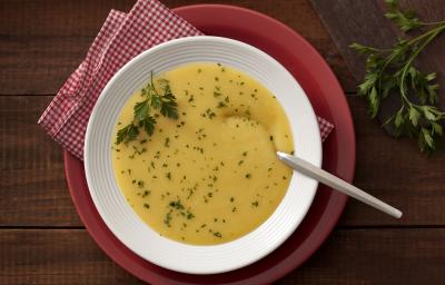 Fotografia em tons de branco, amarelo e vermelho, com prato branco ao centro contendo um creme amarelo com salsa e uma colher sobre guardanapo quadriculado em vermelho e branco e sous plat vermelho, ramo de salsa, e tudo sobre bancada de madeira rústica. Fotografia em tons de branco, amarelo e vermelho, com prato branco ao centro contendo um creme amarelo com salsa e uma colher sobre guardanapo quadriculado em vermelho e branco e sous plat vermelho, ramo de salsa, e tudo sobre bancada de madeira rústica.
