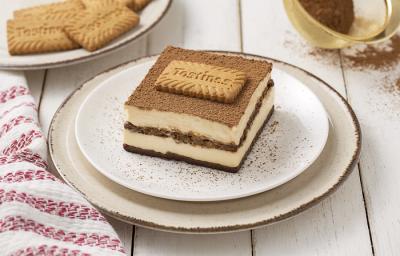 Foto da receita de Tiramisú de Tostines Especiarias. Observa-se uma fatia do Tiramisú bem alta expondo as camadas de creme e de biscoito. No topo, observa-se cacau em pó polvilhado com um Biscoito Tostines. Foto da receita de Tiramisú de Tostines Especiarias. Observa-se uma fatia do Tiramisú bem alta expondo as camadas de creme e de biscoito. No topo, observa-se cacau em pó polvilhado com um Biscoito Tostines.