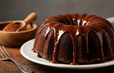 Um bolo de chocolate Bundt, rico e úmido, é apresentado em um prato cerâmico branco. Coberto com um brilho de chocolate cremosa, o bolo exibe uma textura macia e escura. Um bolo de chocolate Bundt, rico e úmido, é apresentado em um prato cerâmico branco. Coberto com um brilho de chocolate cremosa, o bolo exibe uma textura macia e escura.