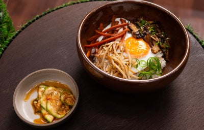 Bibimbap vegetariano com arroz japonês, legumes coloridos salteados e ovo de gema mole, acompanhado de molho picante
