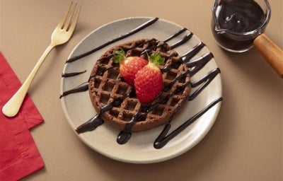 Fotografia de um prato de vidro com o waffle, dois morangos inteiros e a calda de nescau. Fotografia de um prato de vidro com o waffle, dois morangos inteiros e a calda de nescau.