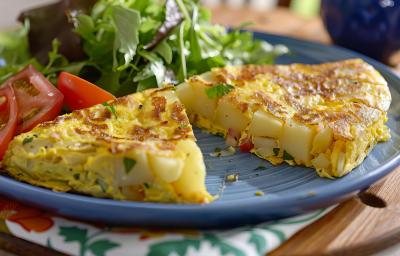 Foto aproximada da receita de omelete com batata, servida em um prato e dividia ao meio, podendo ver as batatas no centro. No prato há uma salada verde e algumas fatias de tomate Foto aproximada da receita de omelete com batata, servida em um prato e dividia ao meio, podendo ver as batatas no centro. No prato há uma salada verde e algumas fatias de tomate