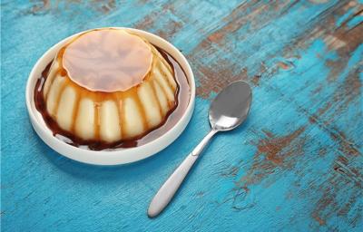 A imagem mostra um Pudim de Tapioca Simples cremoso, com uma textura suave e um caramelo dourado brilhante por cima. O pudim é servido em uma forma elegante, destacando sua cor branca e a consistência delicada.