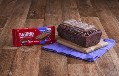 Foto da Receita de Bolo de Chocolate com Cobertura de Choco Trio. Observa-se um bolo em formato inglês sobre uma tábua de madeira e um pano roxo. Foto da Receita de Bolo de Chocolate com Cobertura de Choco Trio. Observa-se um bolo em formato inglês sobre uma tábua de madeira e um pano roxo.