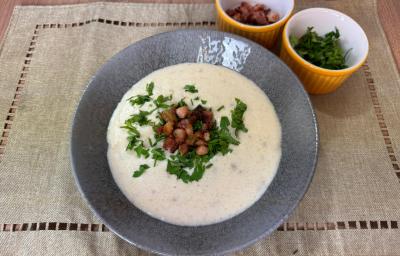 Fotografia em tons claros com um prato cinza ao centro. Em cima do prato existe uma receita de creme de mandioca finalizado com bacon e salsinha Fotografia em tons claros com um prato cinza ao centro. Em cima do prato existe uma receita de creme de mandioca finalizado com bacon e salsinha
