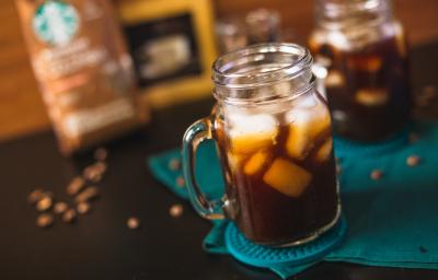 Fotografia em tons de preto de uma bancada preta, com um paninho verde e dois copos com alça com gelo e café. Fotografia em tons de preto de uma bancada preta, com um paninho verde e dois copos com alça com gelo e café.
