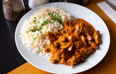 Foto aproximada da receita de strogonoff de carne tradicional, com um molho escuro marrom, pedaços de champignon, servido em um prato branco com arroz e ervas finas picadas