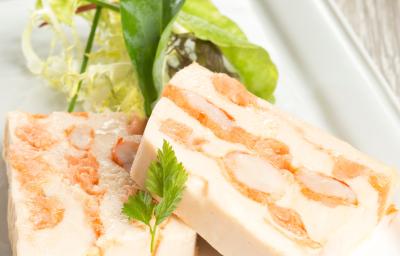 Fotografia de duas fatias de terrine de gorgonzola com nozes e cream cheese sobre um apoio branco retangular.