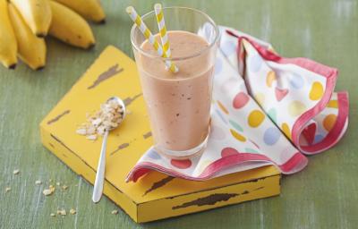 Fotografia em tons de verde e amarelo de uma bancada verde com uma tábua amarela, sobre ela um paninho com bolinhas coloridas e um copo com vitamina de frutas. Ao lado uma colher. Ao fundo um cacho de banana. Fotografia em tons de verde e amarelo de uma bancada verde com uma tábua amarela, sobre ela um paninho com bolinhas coloridas e um copo com vitamina de frutas. Ao lado uma colher. Ao fundo um cacho de banana.