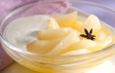 Fotografia em tons de roxo em uma bancada de madeira com toalha roxa, um paninho lilás, um recipiente redondo de vidro com as peras com creme de leite dentro dele. Fotografia em tons de roxo em uma bancada de madeira com toalha roxa, um paninho lilás, um recipiente redondo de vidro com as peras com creme de leite dentro dele.
