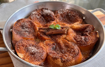 A imagem mostra uma frigideira de alumínio prateada redonda, com rabanadas douradas decoradas com um pau de canela e folhas de hortelã.