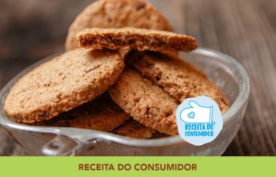 Foto aproximada da receita de Cookies Integrais, dentro de um pote de vidro, em tom marrom claro, sobre uma bancada de madeira e com dizeres no rodapé em tom verde. Foto aproximada da receita de Cookies Integrais, dentro de um pote de vidro, em tom marrom claro, sobre uma bancada de madeira e com dizeres no rodapé em tom verde.