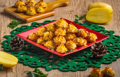 Foto da receita Batatas Natalinas, em tom amarelo e dourado, servidas em um prato vermelho quadrado sobre uma toalha verde natalina. Tudo está em uma mesa de madeira decorada com batatas cruas, pinhas natalinas e mais algumas batatas prontas. Foto da receita Batatas Natalinas, em tom amarelo e dourado, servidas em um prato vermelho quadrado sobre uma toalha verde natalina. Tudo está em uma mesa de madeira decorada com batatas cruas, pinhas natalinas e mais algumas batatas prontas.