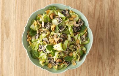 fotografia em tons de bege e verde de uma bancada vista de cima. Ao centro contém um recipiente redondo com salada de abobrinha.
