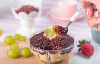 Fotografia em tons de verde com uma taça de vidro ao meio com sobremesa de chocolate e uva dentro.